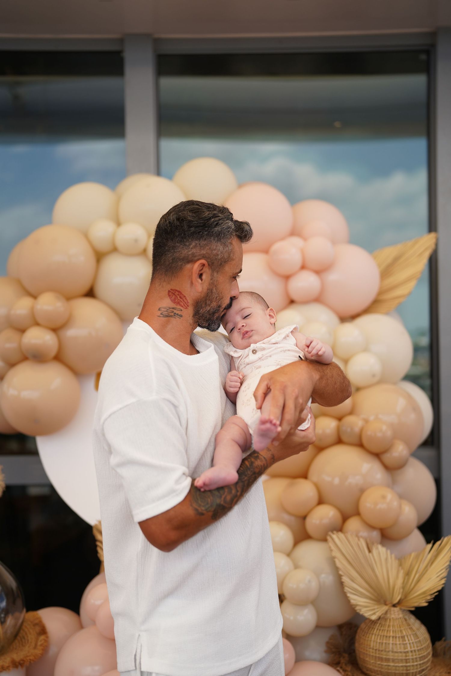A sweet moment with a baby against a backdrop of pastel balloon decorations and dried palm leaves.