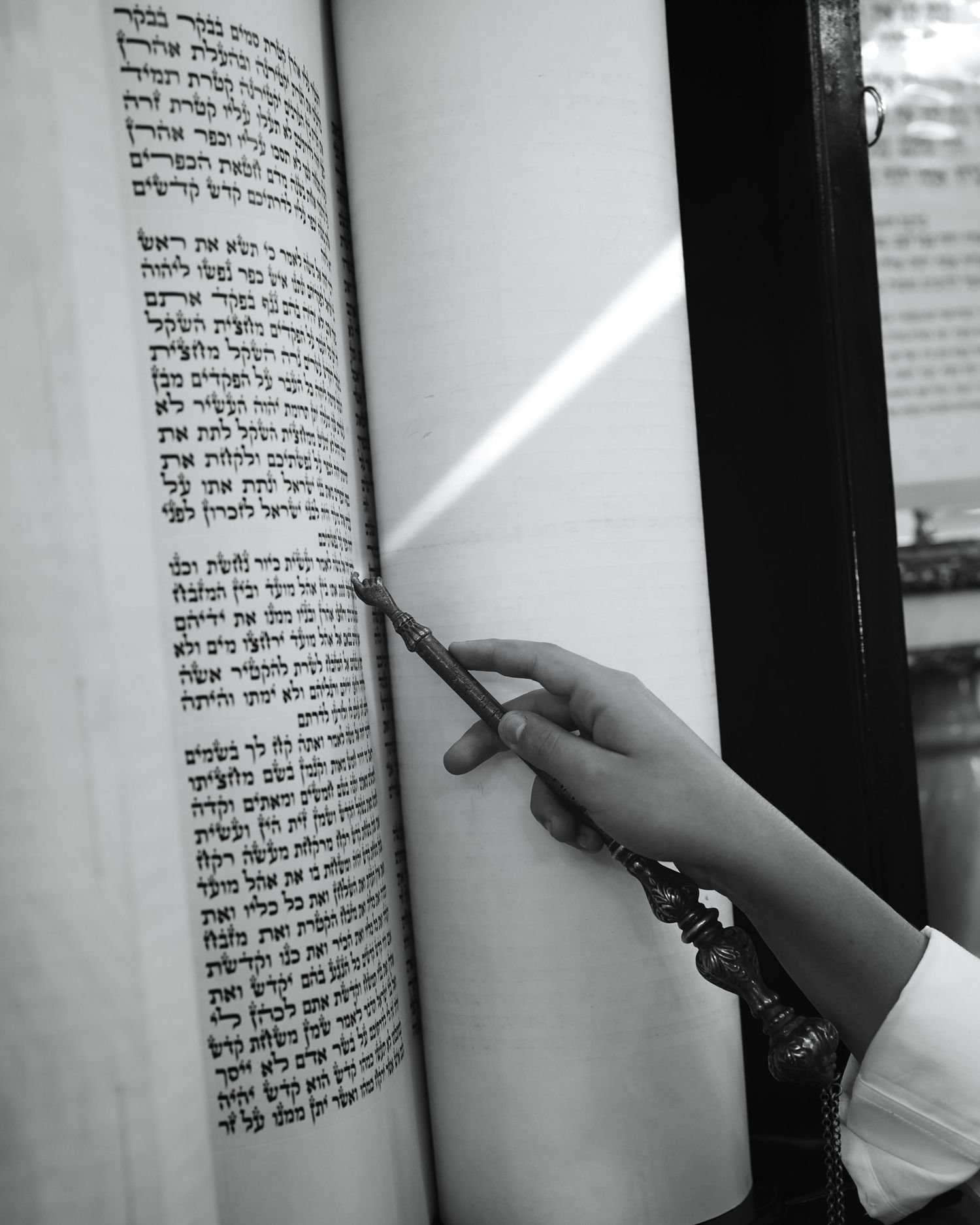 A hand points to Hebrew text in a Torah scroll with a silver yad pointer.