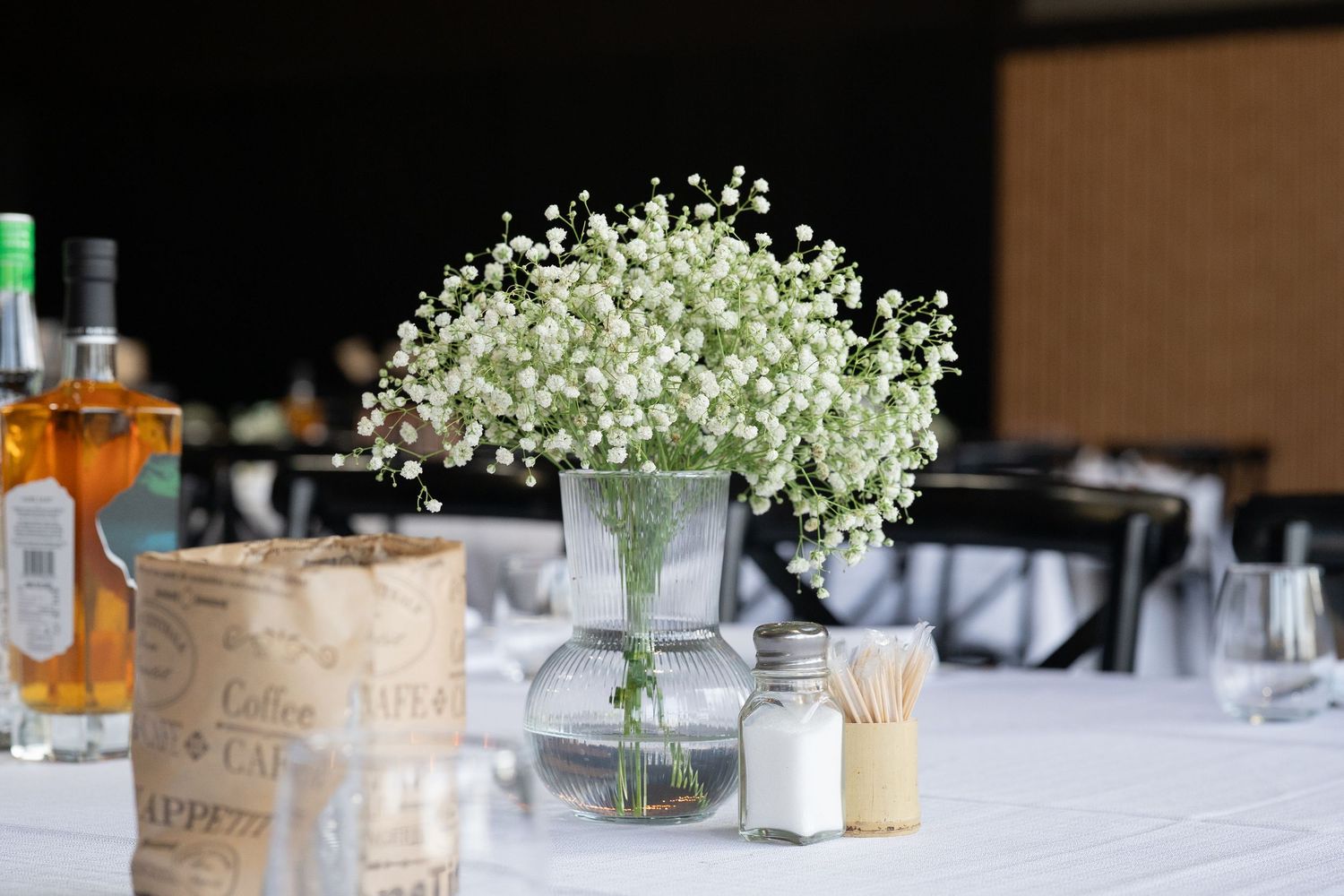 Table setting with baby's breath centerpiece and bottles on white tablecloth.