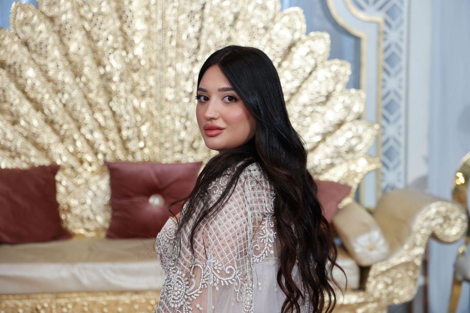 An elegant portrait against a decorative gold fan backdrop in formal attire.