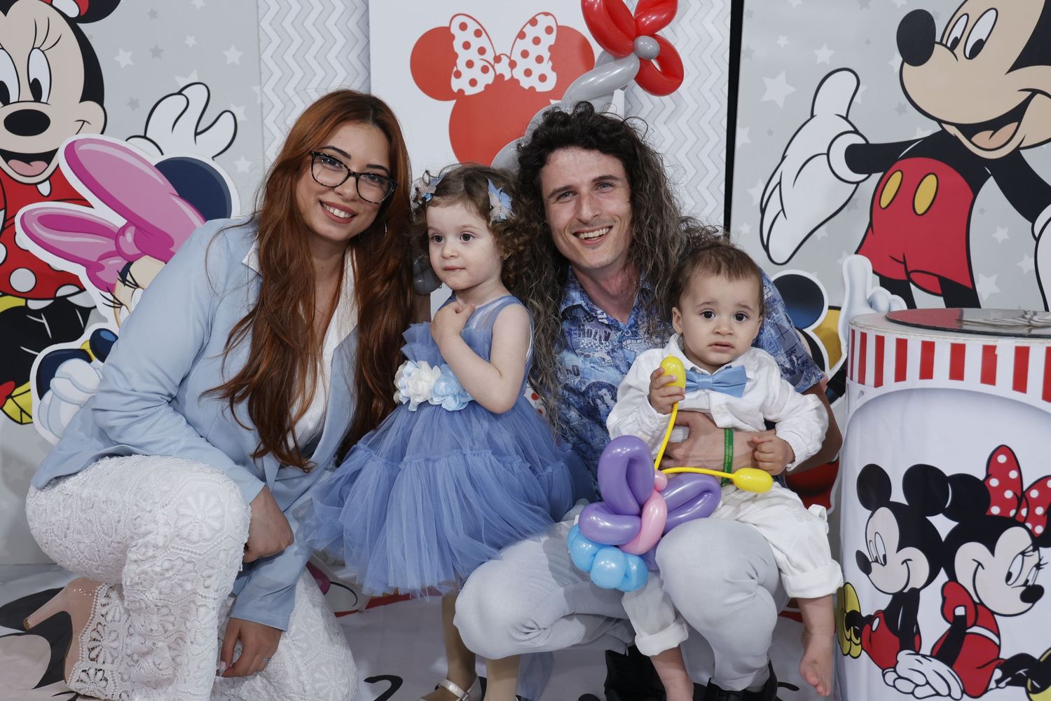 A family photo session with Mickey Mouse themed backdrop and party decorations.
