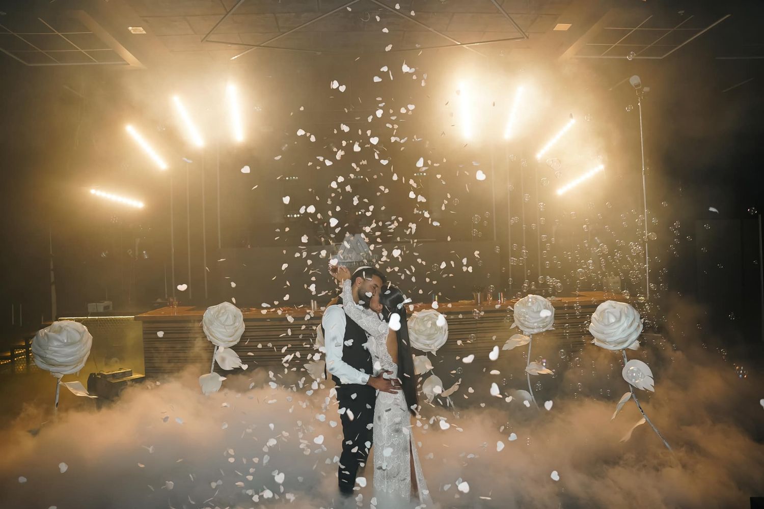 Wedding celebration with confetti falling under warm golden venue lighting.