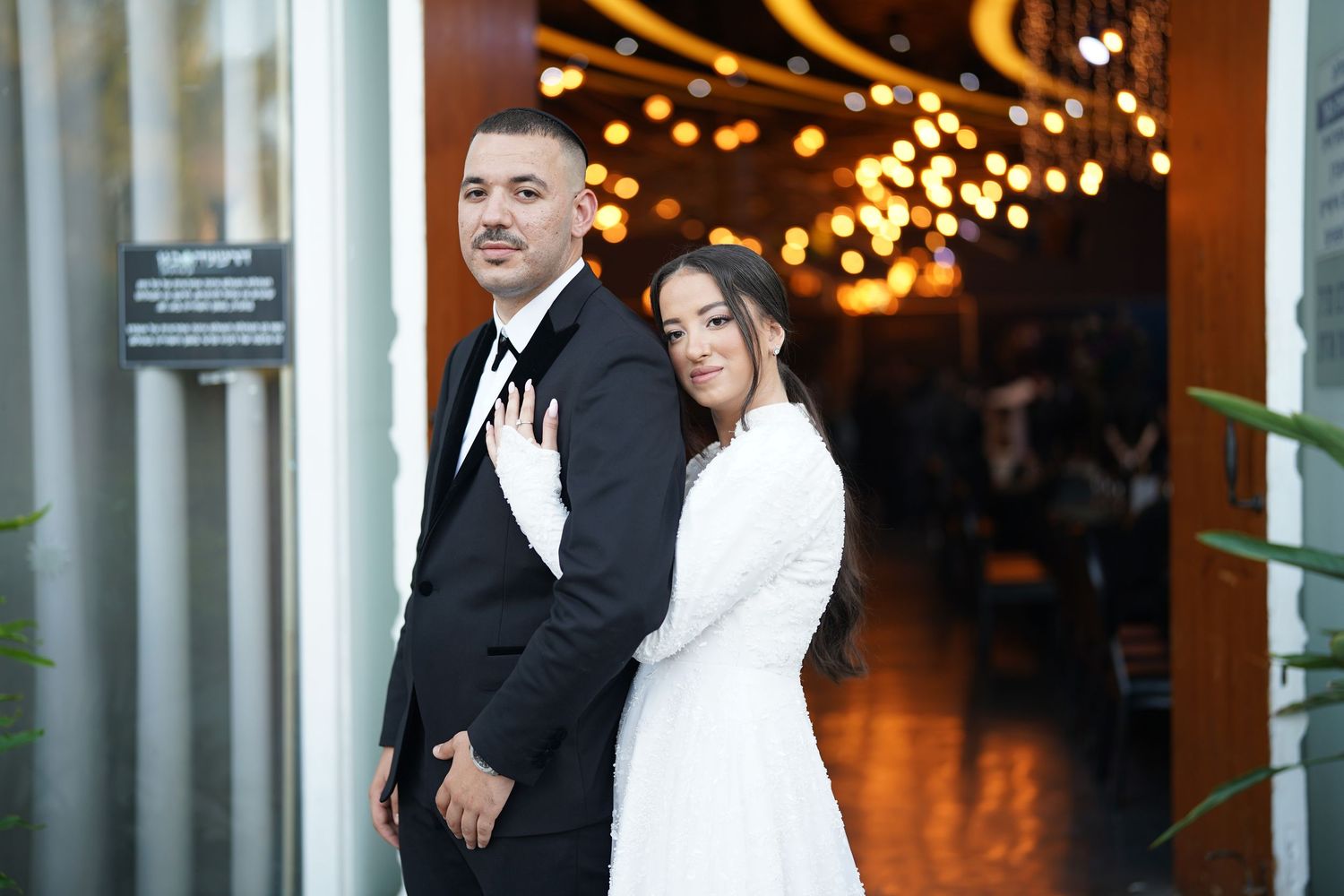 Newlyweds share an intimate moment under twinkling lights during their first dance at an elegant indoor reception.