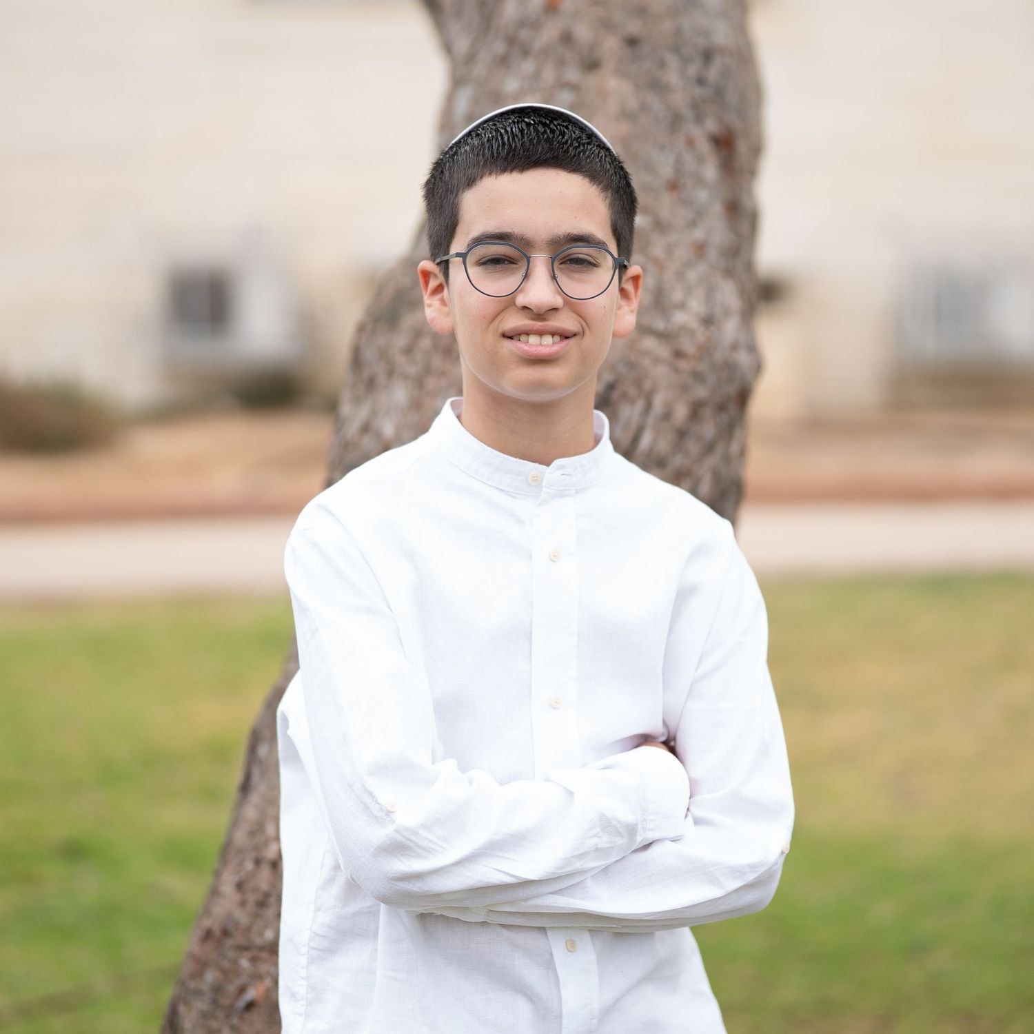 A person in white clothing poses outdoors in a grassy field.