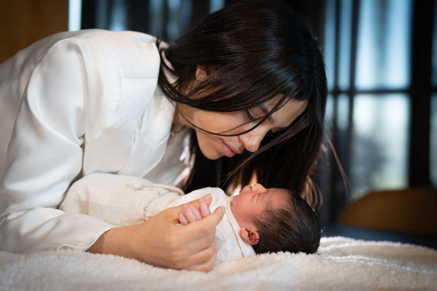 An intimate moment between parent and newborn baby on white bedding.