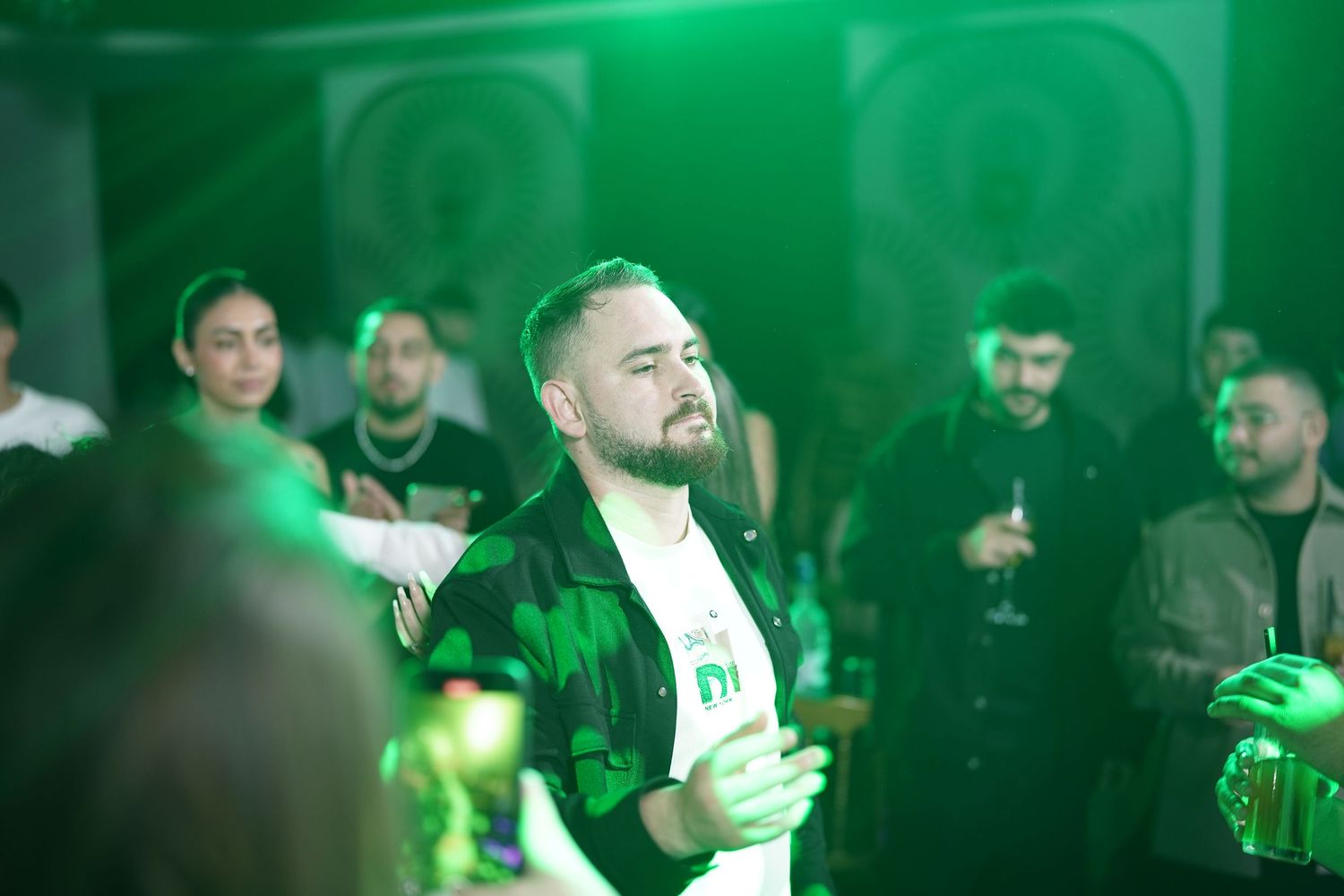 People enjoying a nightclub atmosphere with green lighting effects and beverages in hand.