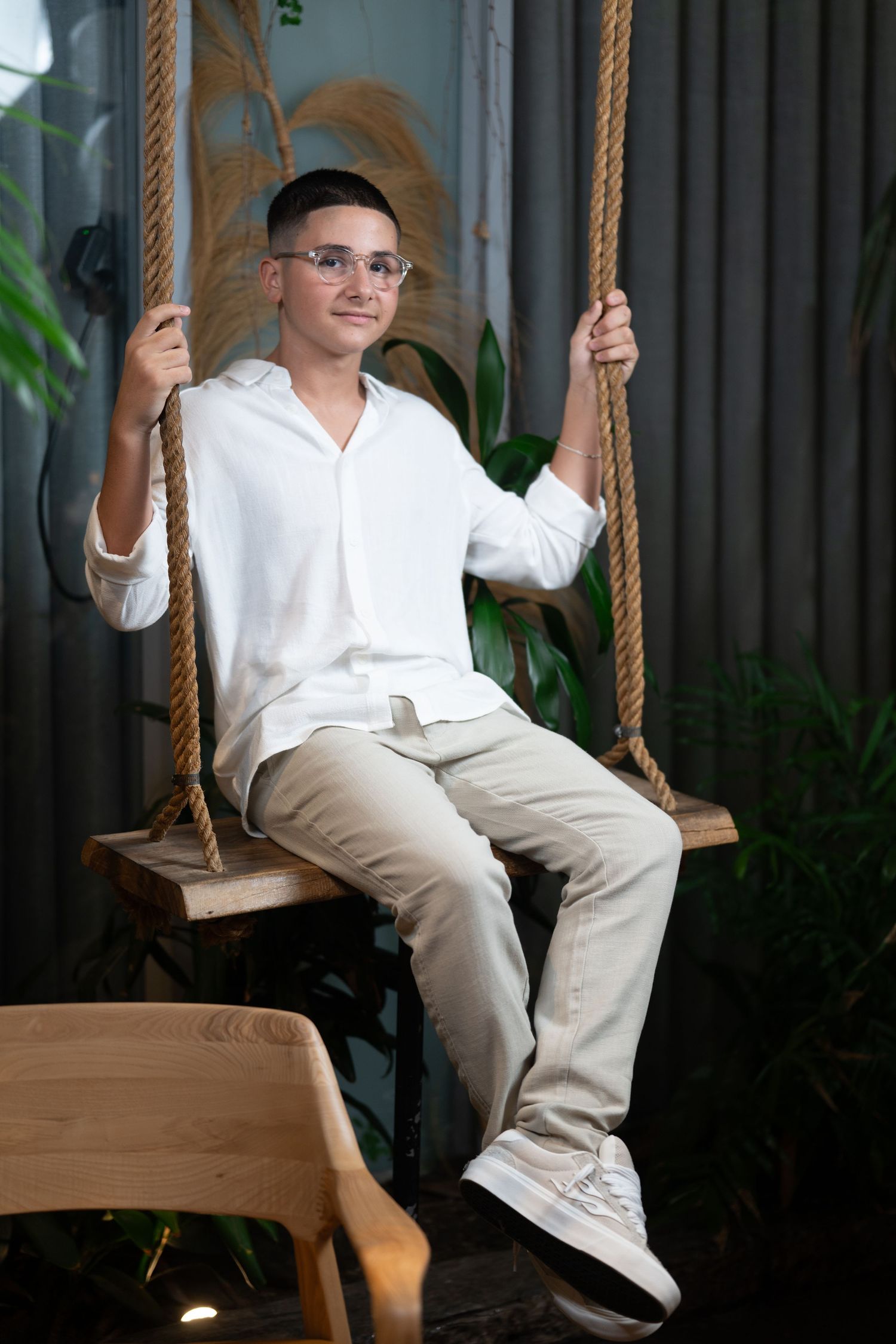 Indoor portrait on wooden rope swing with greenery and modern decor.