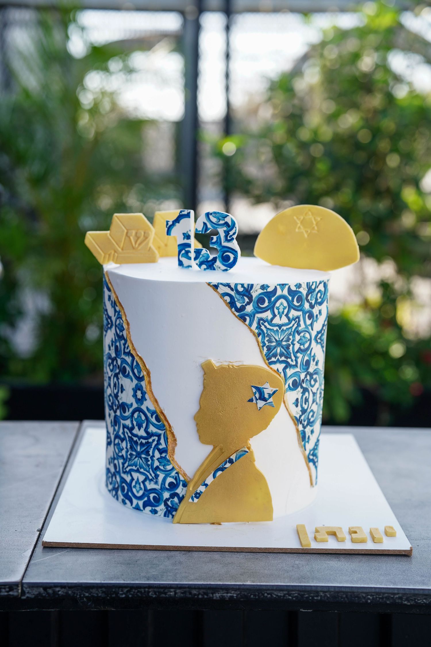 Elegant white and blue decorated cake with gold accents on display table.
