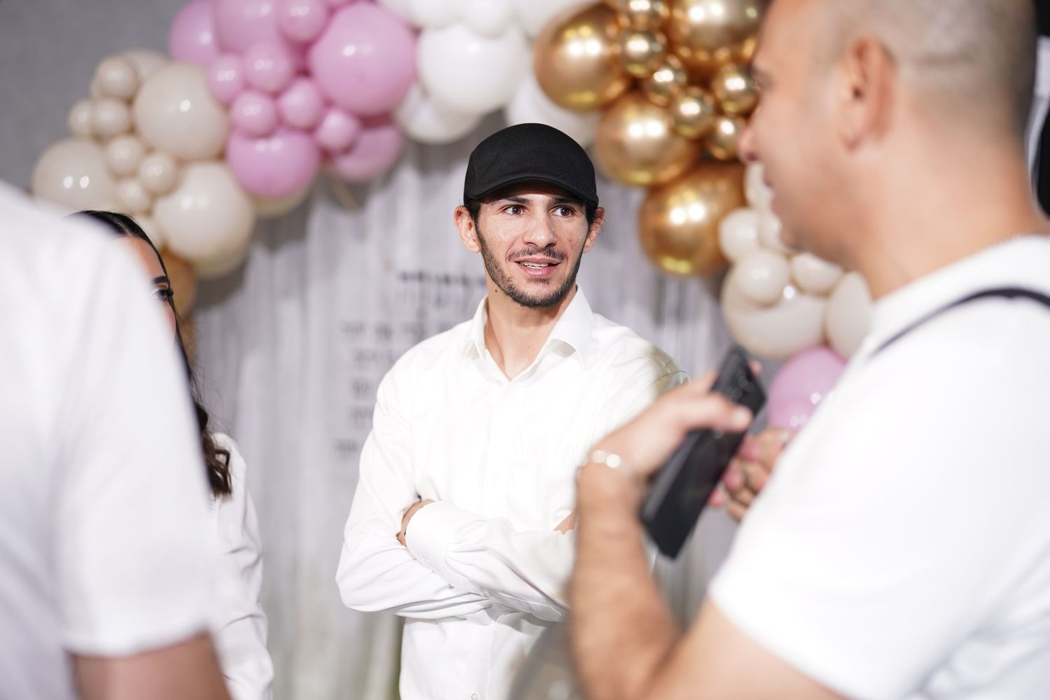 Casual conversation at celebration event with decorative balloon arch in background.