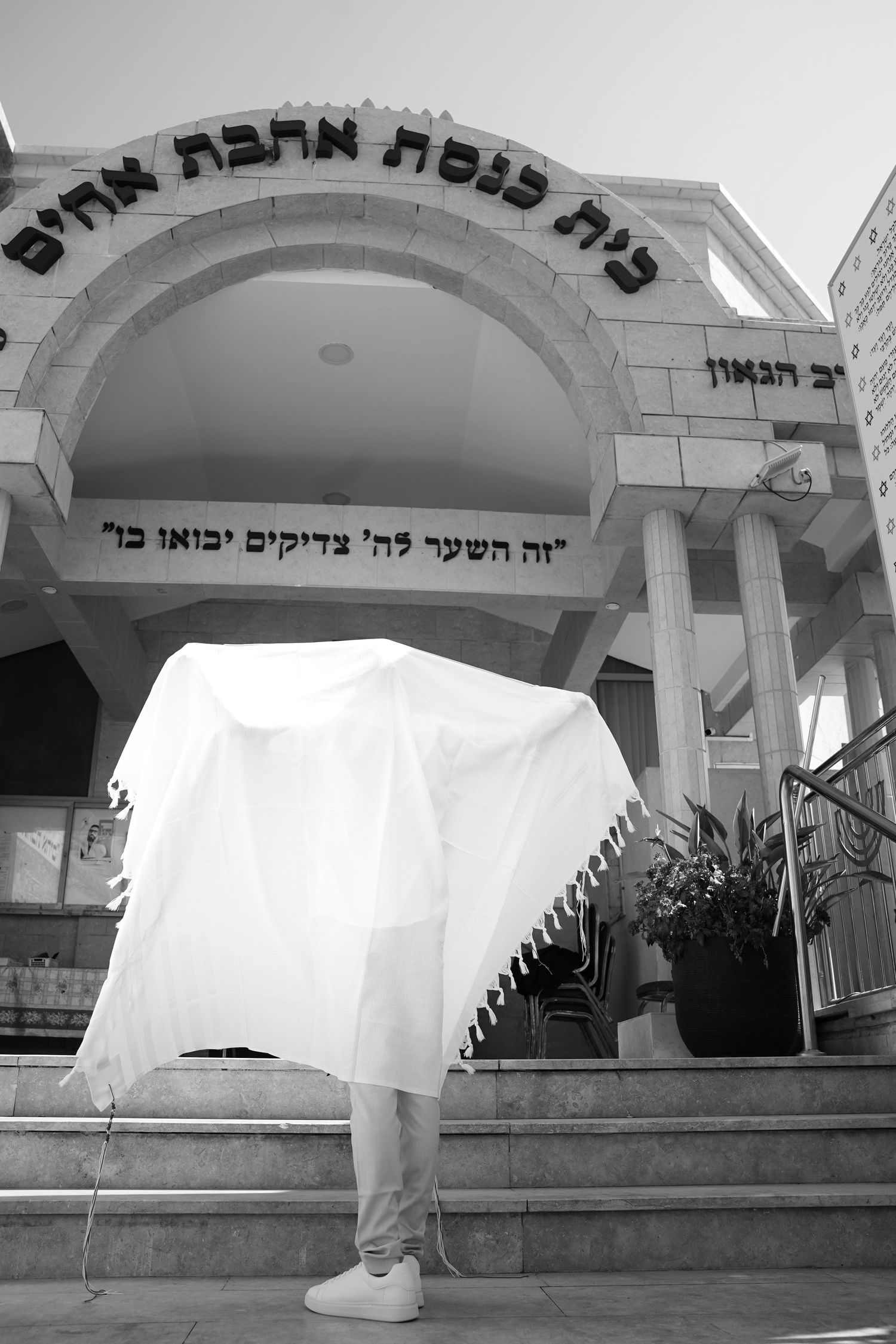 Person wrapped in white tallit prayer shawl standing on steps of Jewish synagogue in Israel.