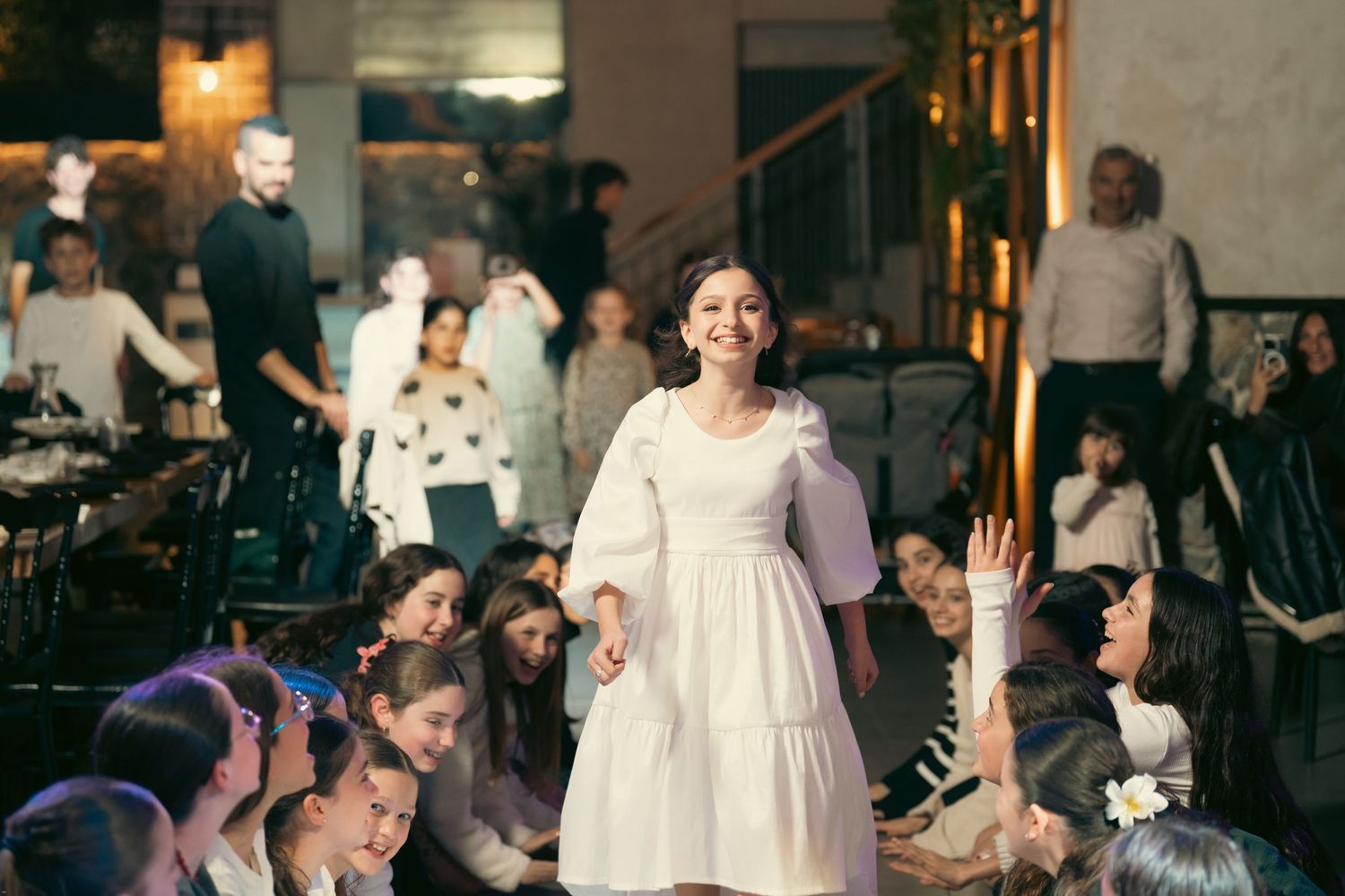 A person in a white dress performs on stage while an audience sits on the floor watching the show.