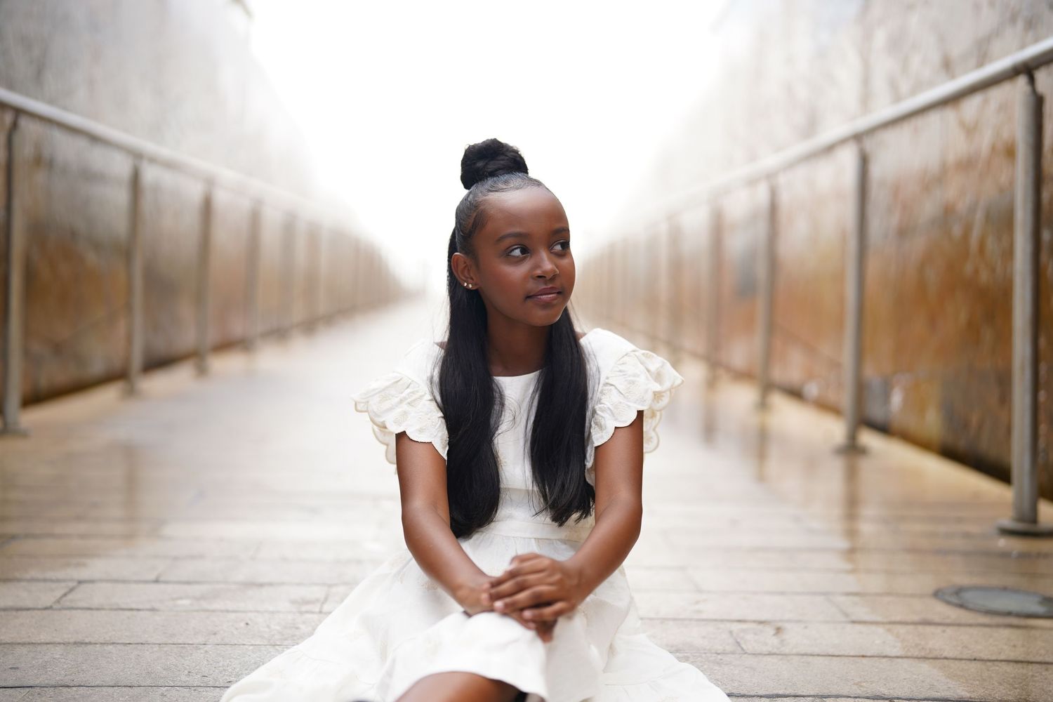 A person in white clothing sits on the ground in a long corridor with dramatic lighting.