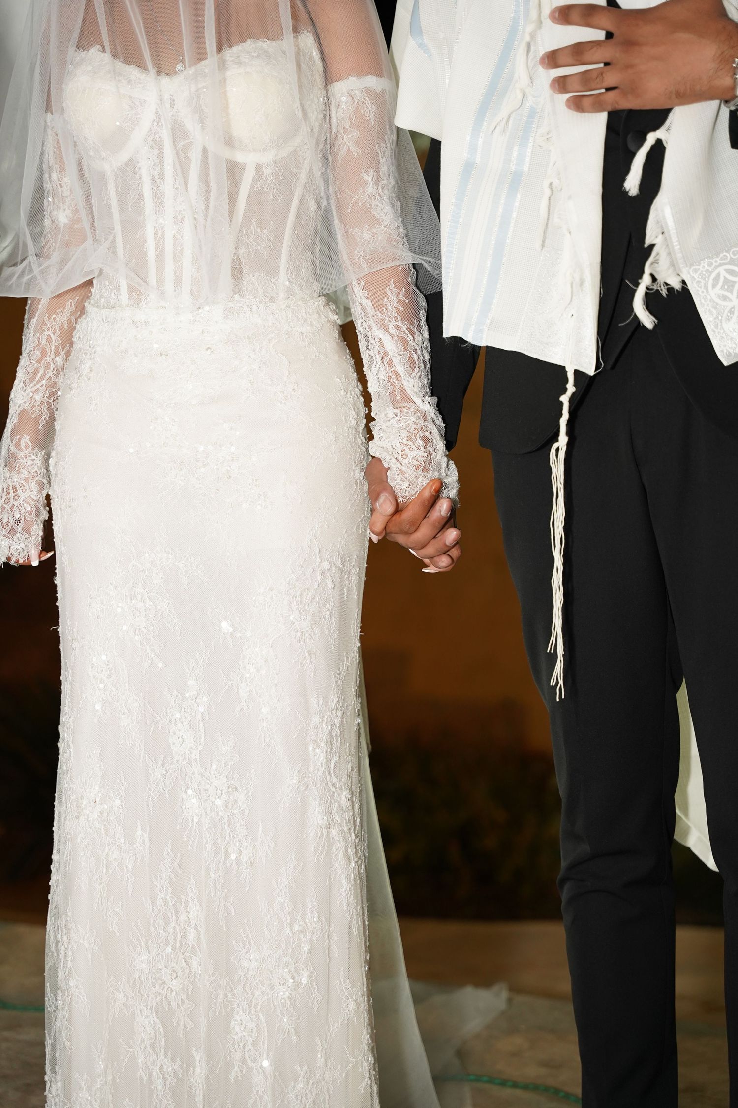 Detail shot of an elegant white lace wedding dress and formal attire during an intimate moment.