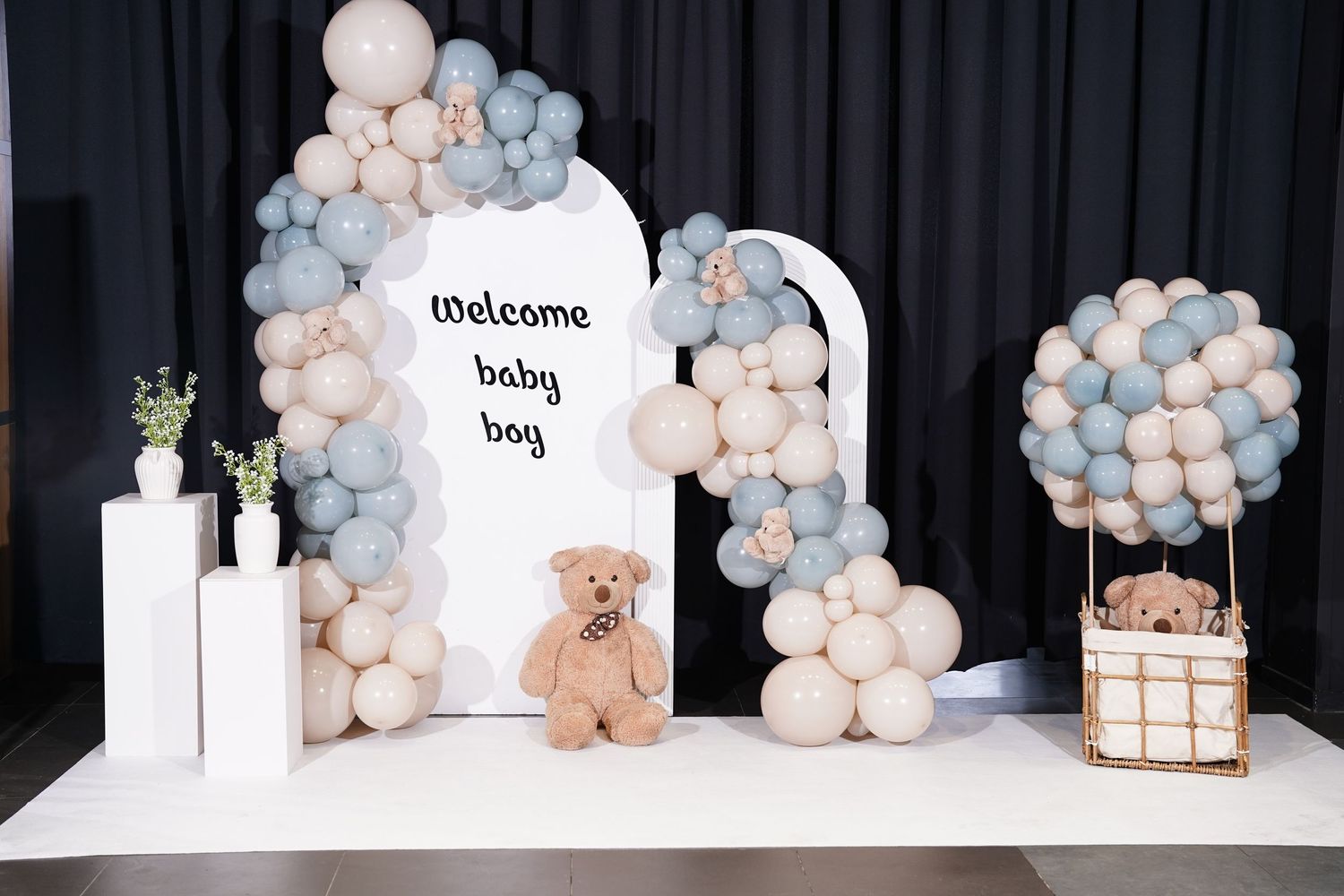 Baby shower decorations featuring pink and blue balloon arches with teddy bear accents.