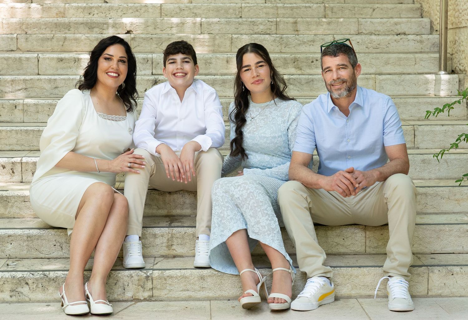 Family members seated on outdoor stone steps in casual white and blue attire.