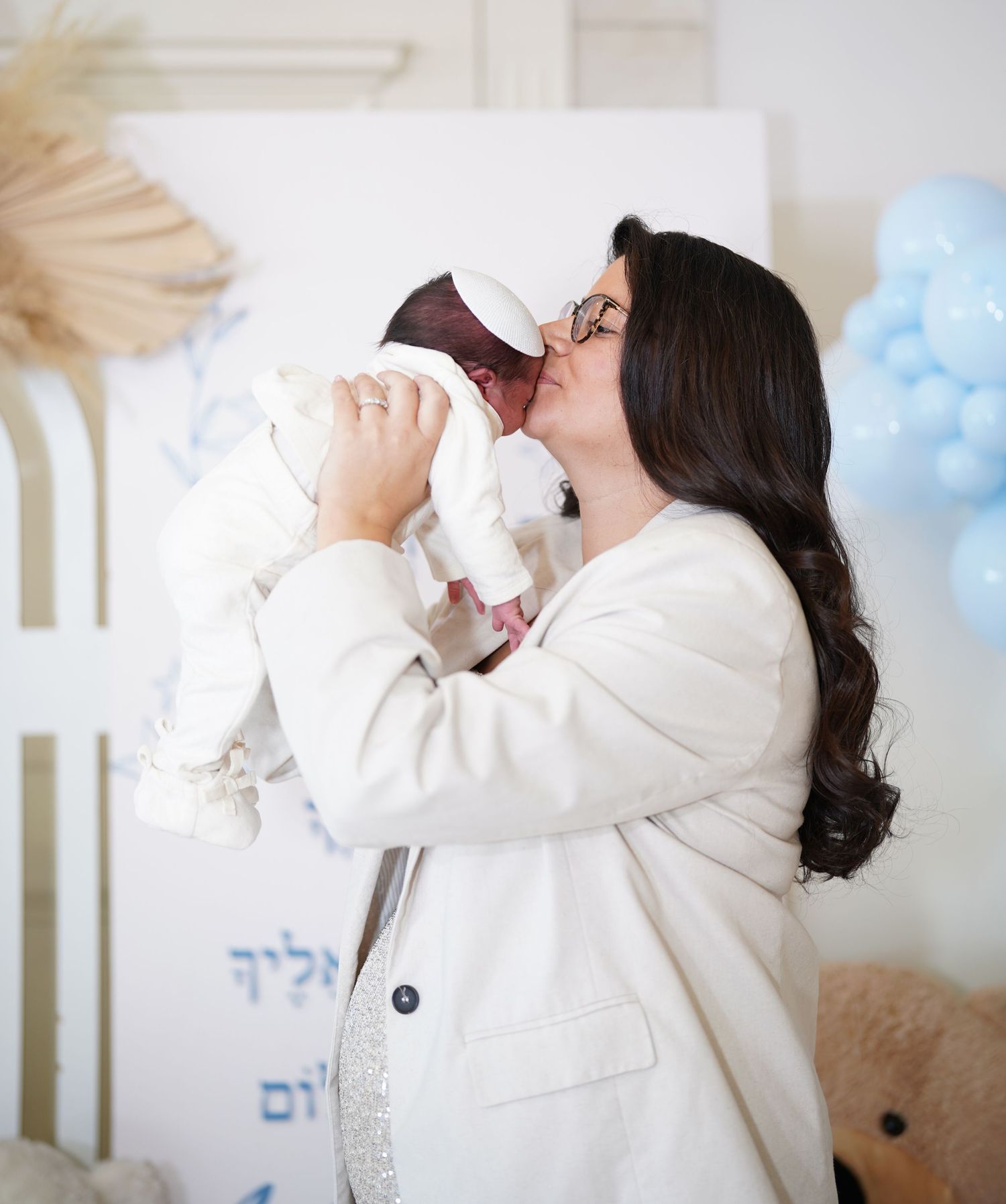 Tender moment between parent and baby against white backdrop with blue balloons.