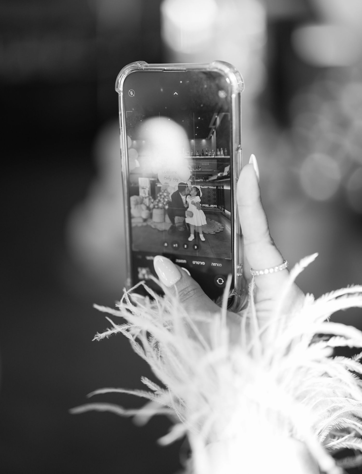 Black and white photo showing mobile phone screen with white feather decoration.