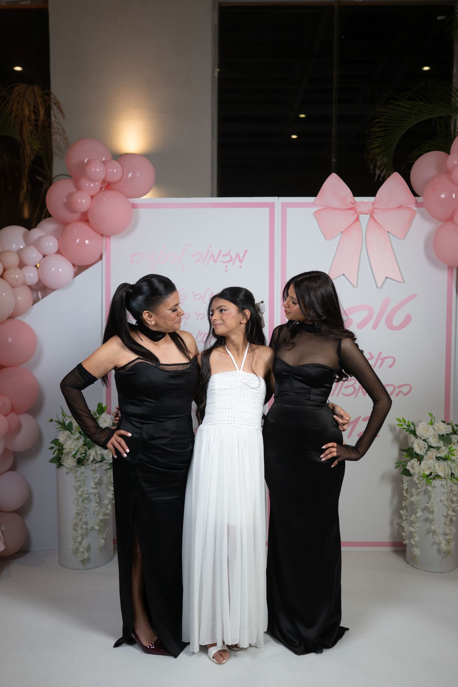 People in black and white attire posing together against a pink balloon-decorated backdrop.