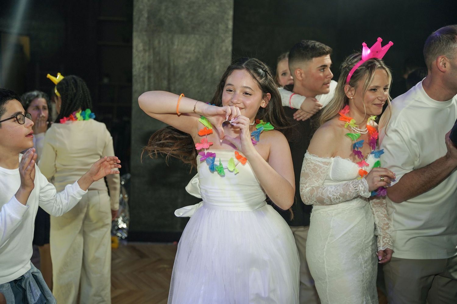 Wedding guests in formal attire dance and celebrate on the dance floor at a reception party.