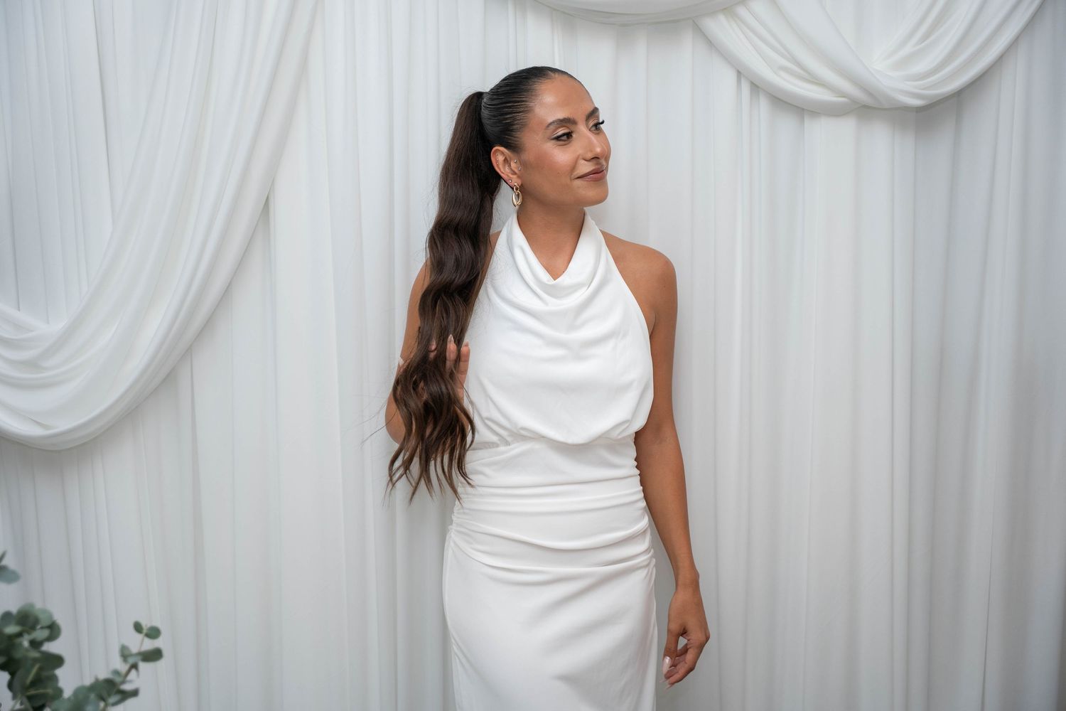 Elegant woman in white sleeveless dress photographed against white draped backdrop.