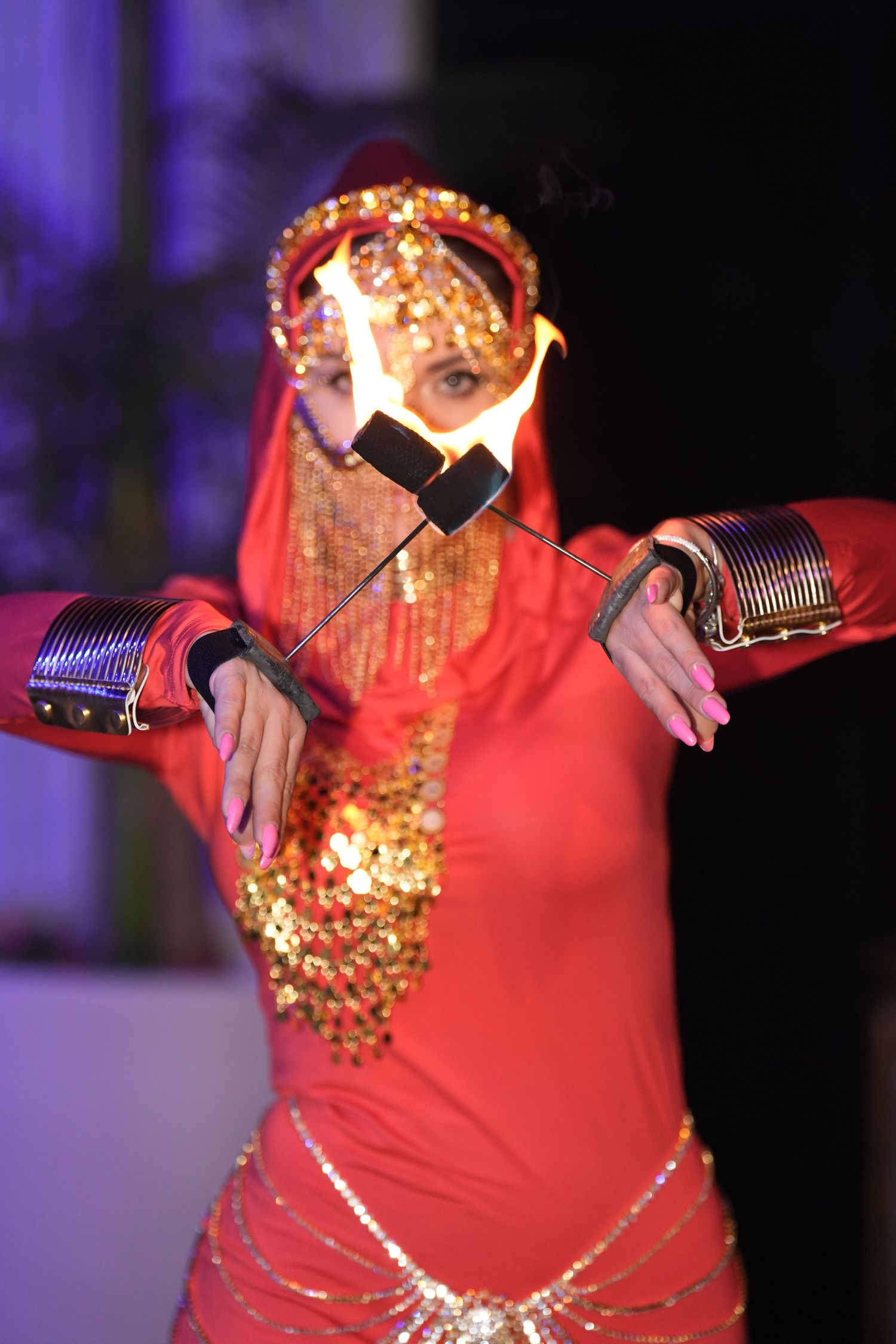 Woman in red belly dance costume with gold accessories performing a fire dance routine on stage.