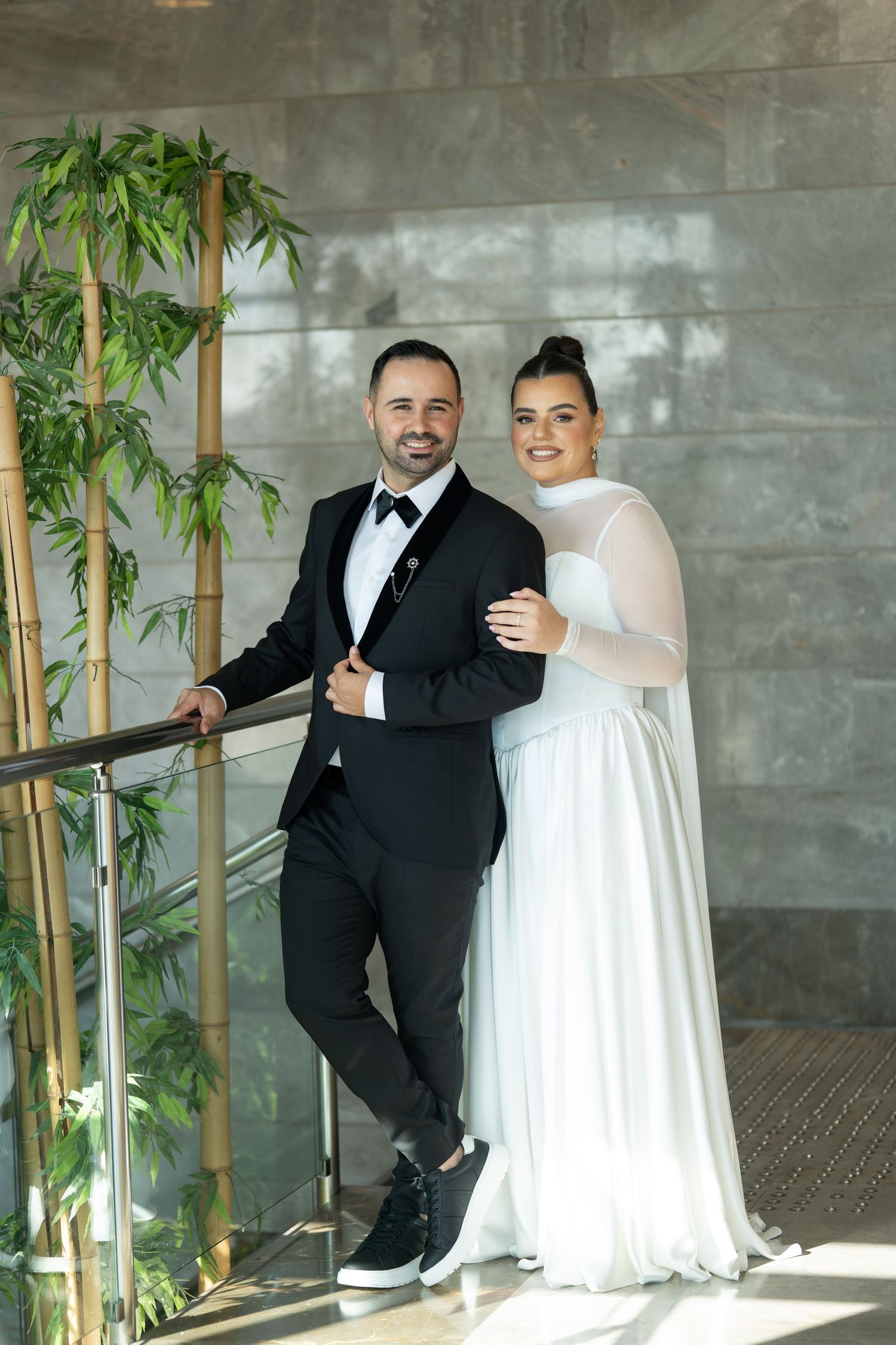 Modern wedding portrait with bamboo plants and contemporary concrete wall backdrop.