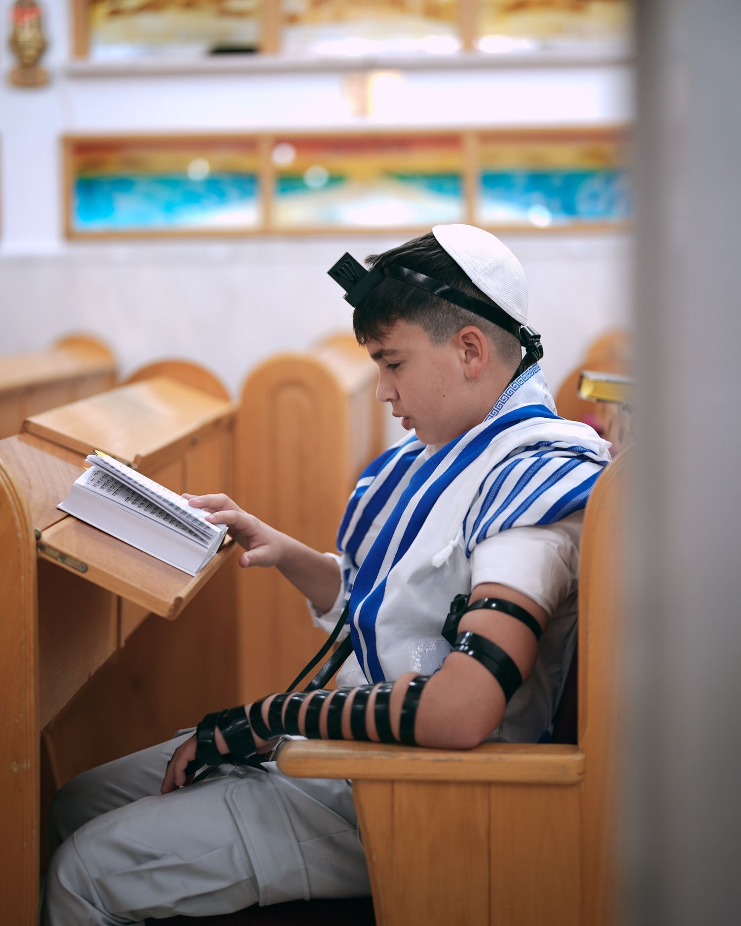 Side view of someone reading from a religious text while wearing traditional Jewish prayer garments.