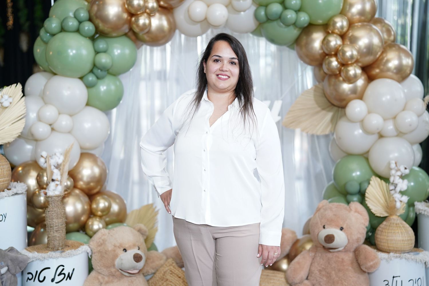 Baby shower setup with teddy bears and balloon decorations in gold, white and sage green colors.