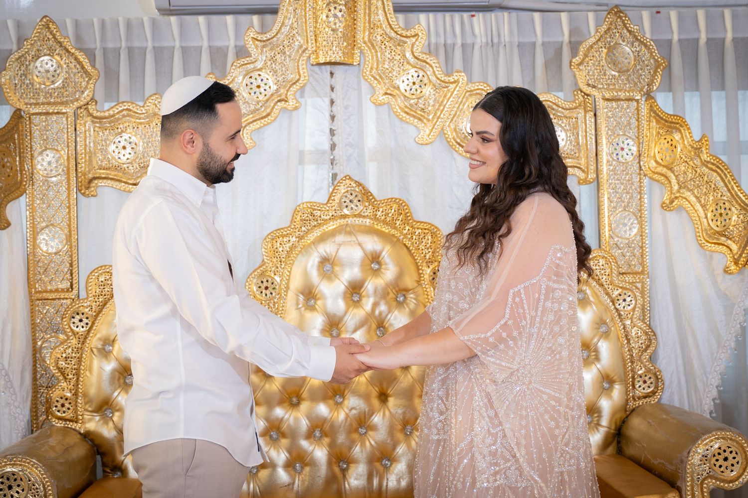 Couple shares tender moment in front of luxurious gold and white backdrop.