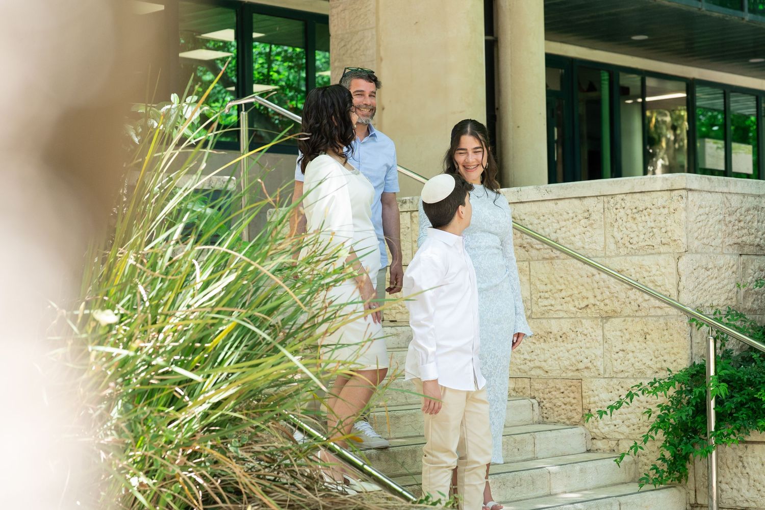 Family photo session on stone steps with architectural elements and plants in background.