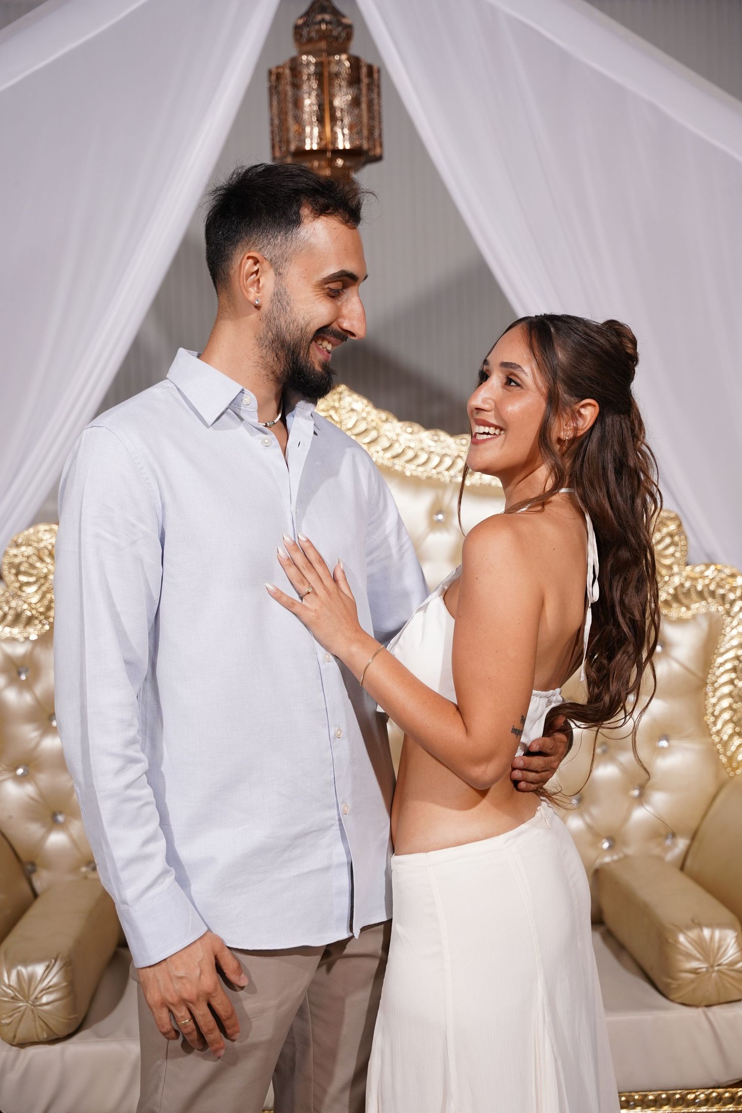 Couple sharing joyful moments in white attire against an elegant backdrop with white draping.