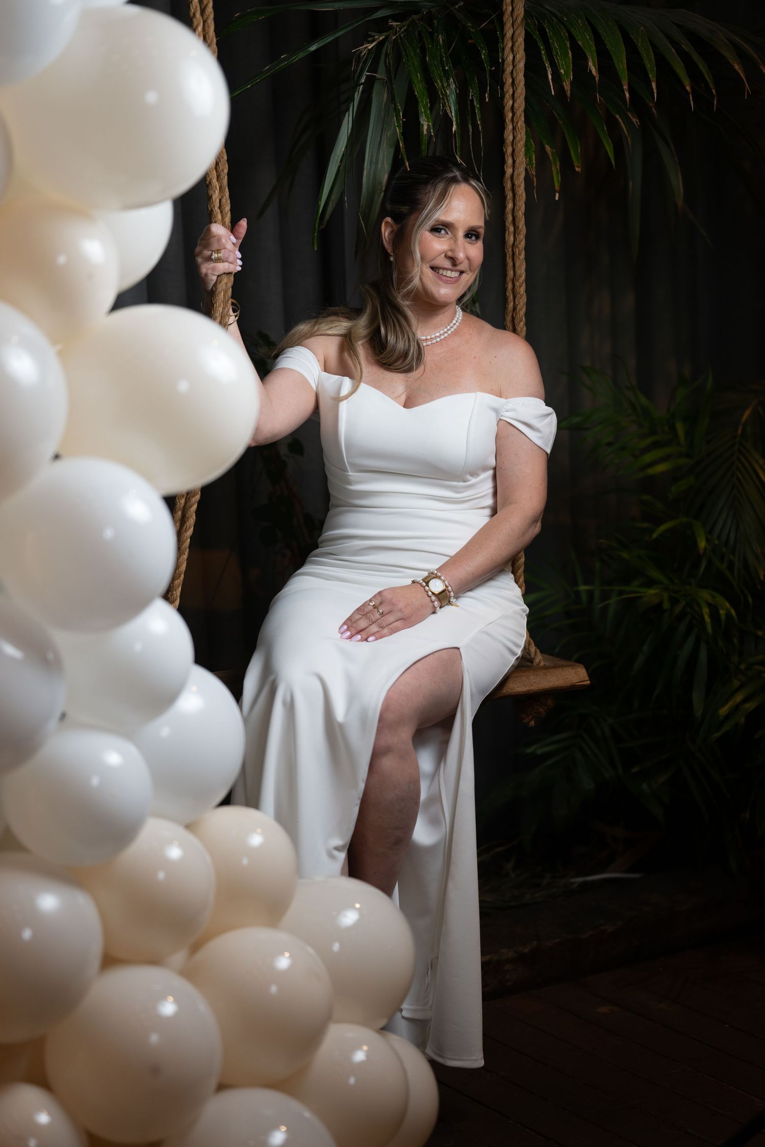 Elegant event setup with white balloon decorations and tropical plants in dimly lit venue.