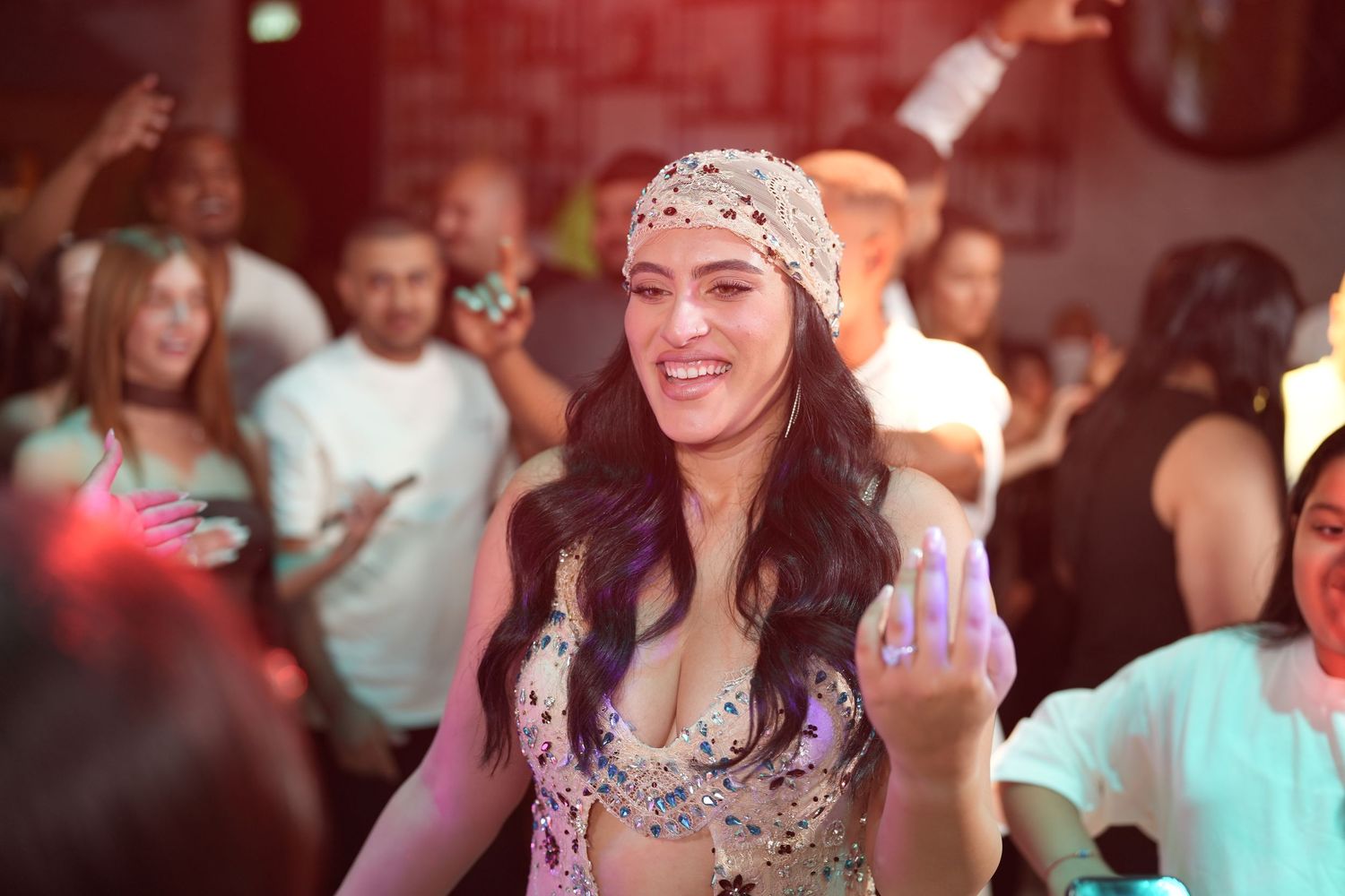Woman in bejeweled costume dancing at a lively party with crowd in background.
