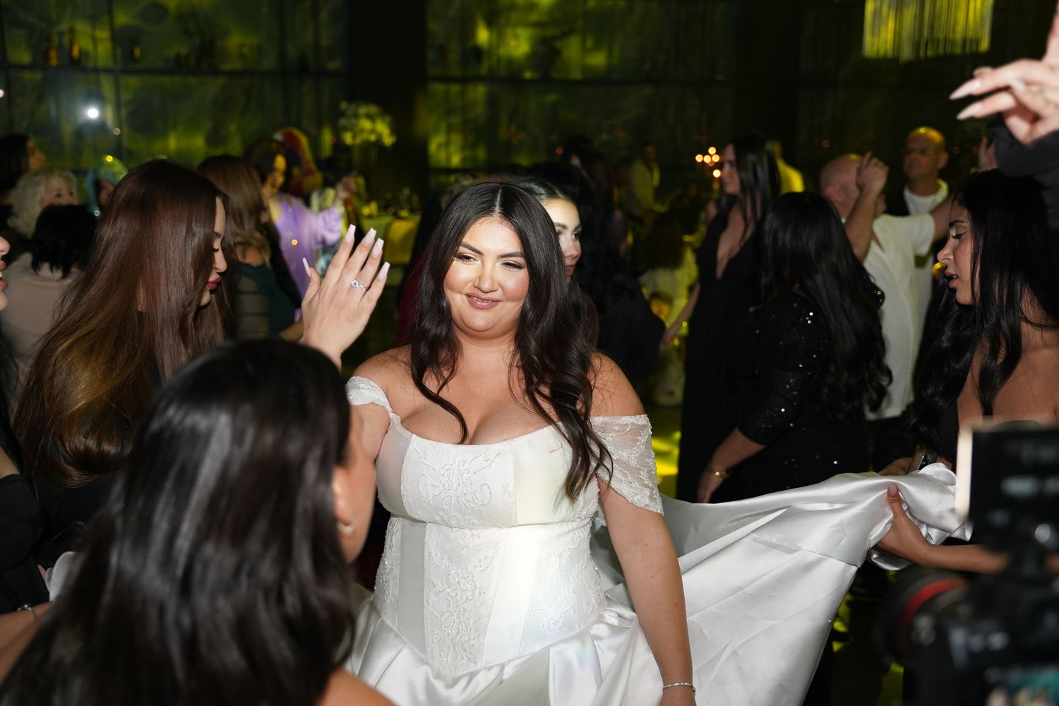 Bride in white wedding dress smiling and dancing with guests at elegant wedding reception celebration.
