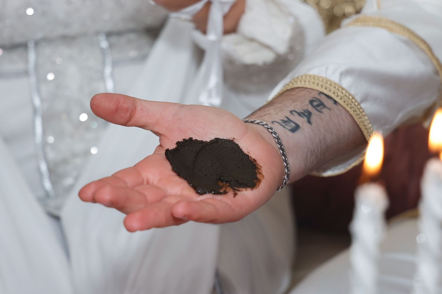 A hand holding dark powder or spices during a traditional ceremony.