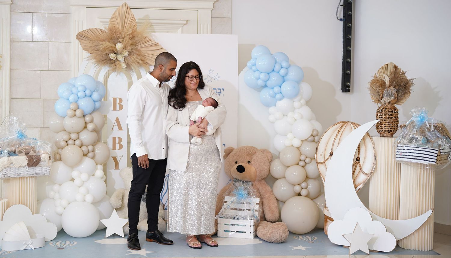 Family photo session with balloon decorations and Hebrew text on wall.