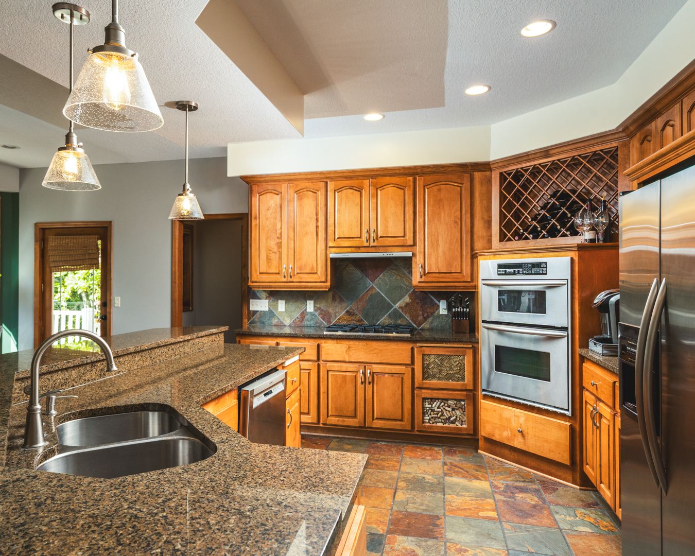 Modern kitchen with honey oak cabinets, granite countertops, pendant lights, and slate tile flooring.