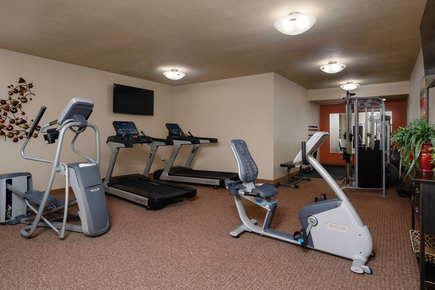 Hotel fitness center with treadmills, elliptical, recumbent bike, and weight machines on carpeted floors.