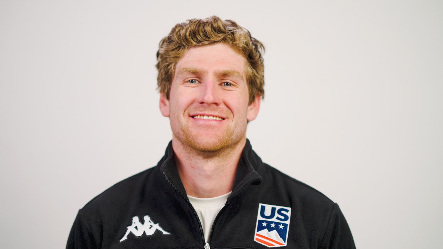 Portrait of athlete in black Kappa jacket with US team logo against white background.