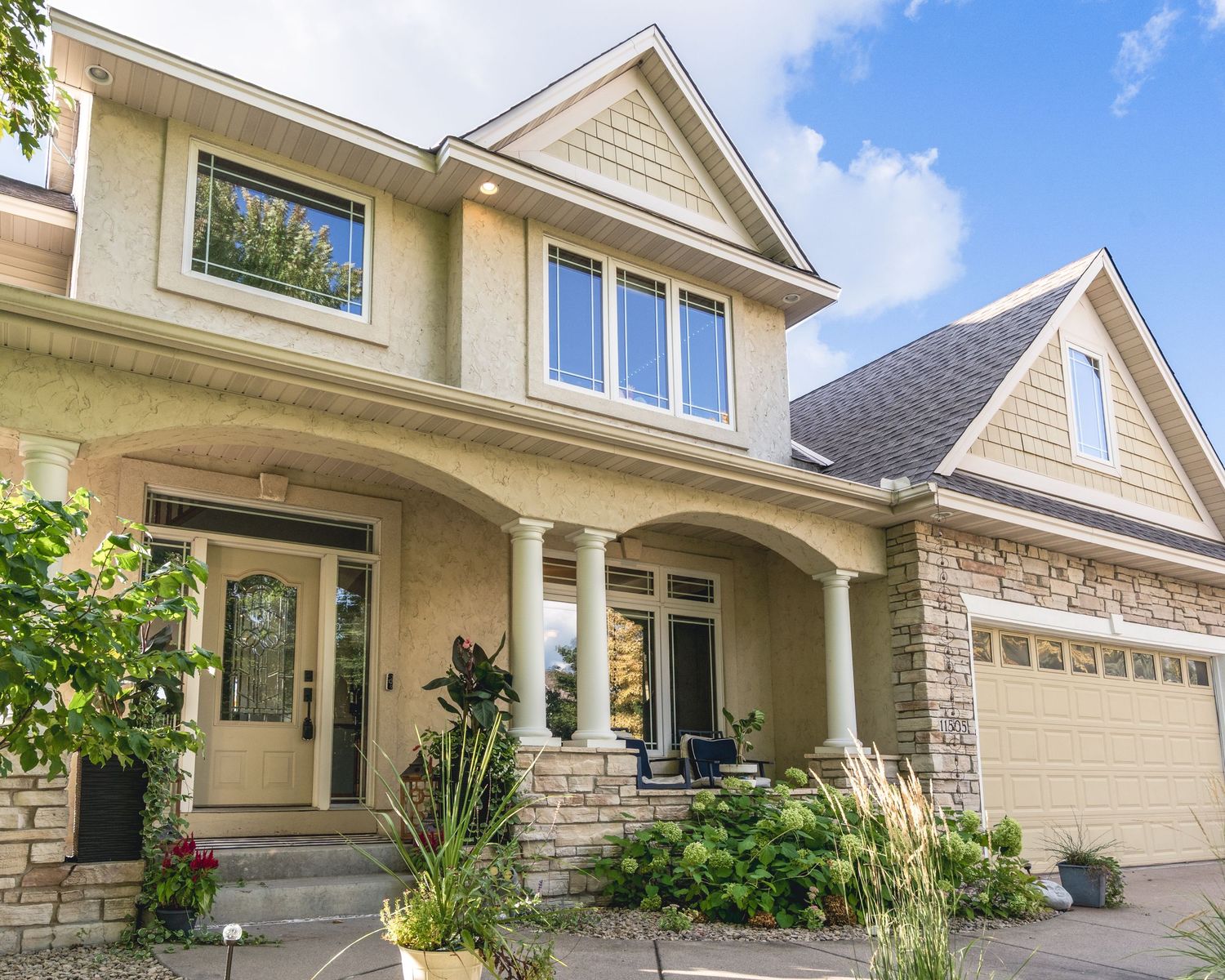 Modern beige and stone exterior of a luxury residential home with large windows and covered entry porch.