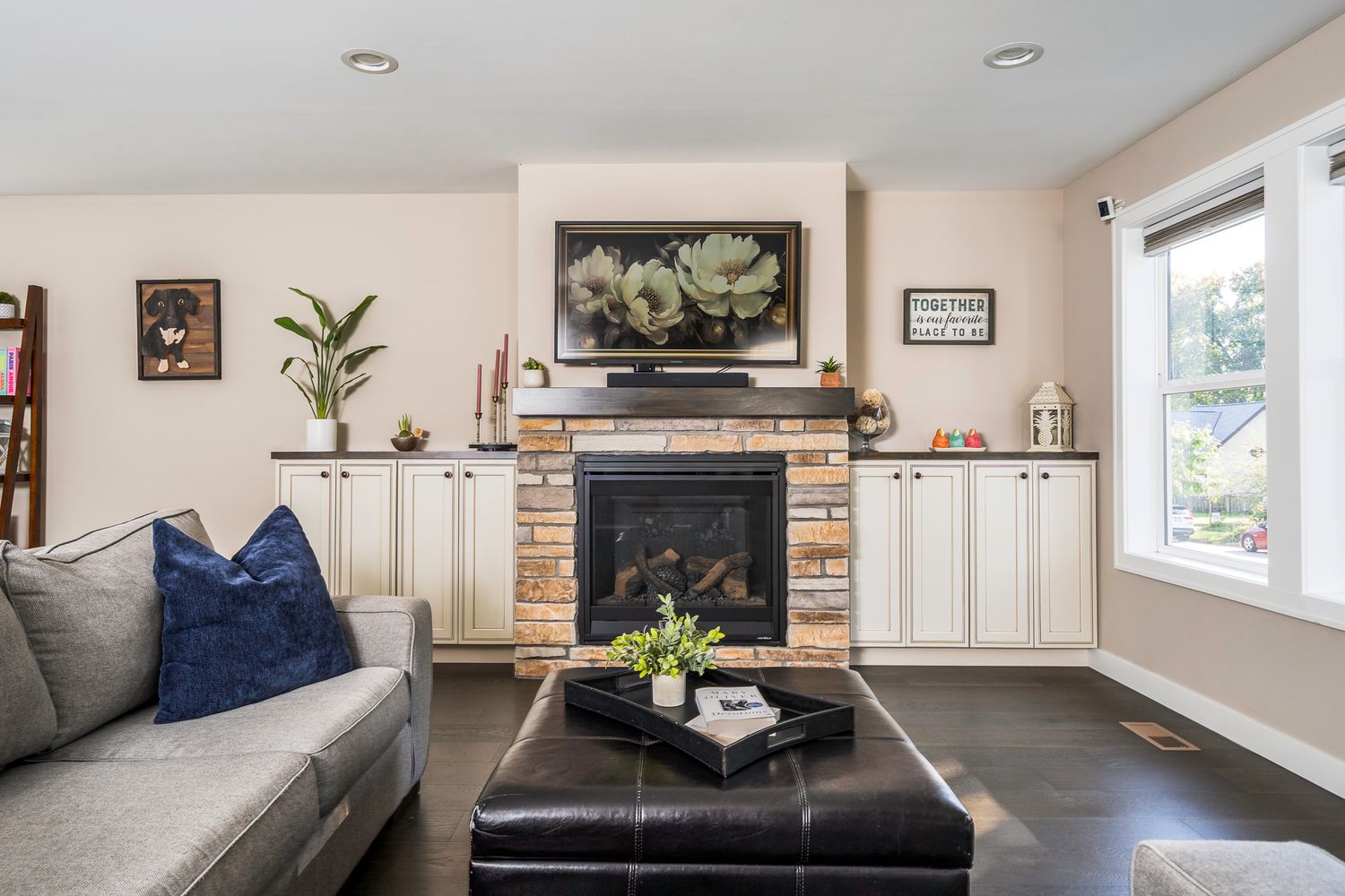 Cozy living room with stone fireplace, white built-ins, gray sofa, navy pillow, and dark hardwood floors.