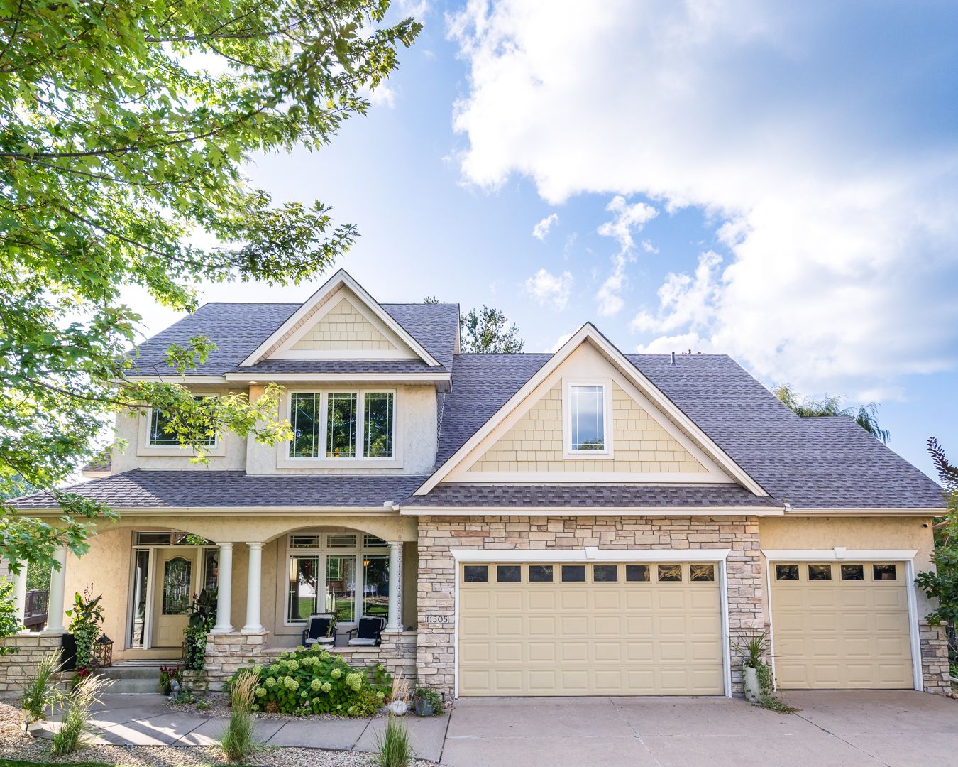 Elegant two-story craftsman house with stone accents, beige siding, and a three-car garage on a sunny day.