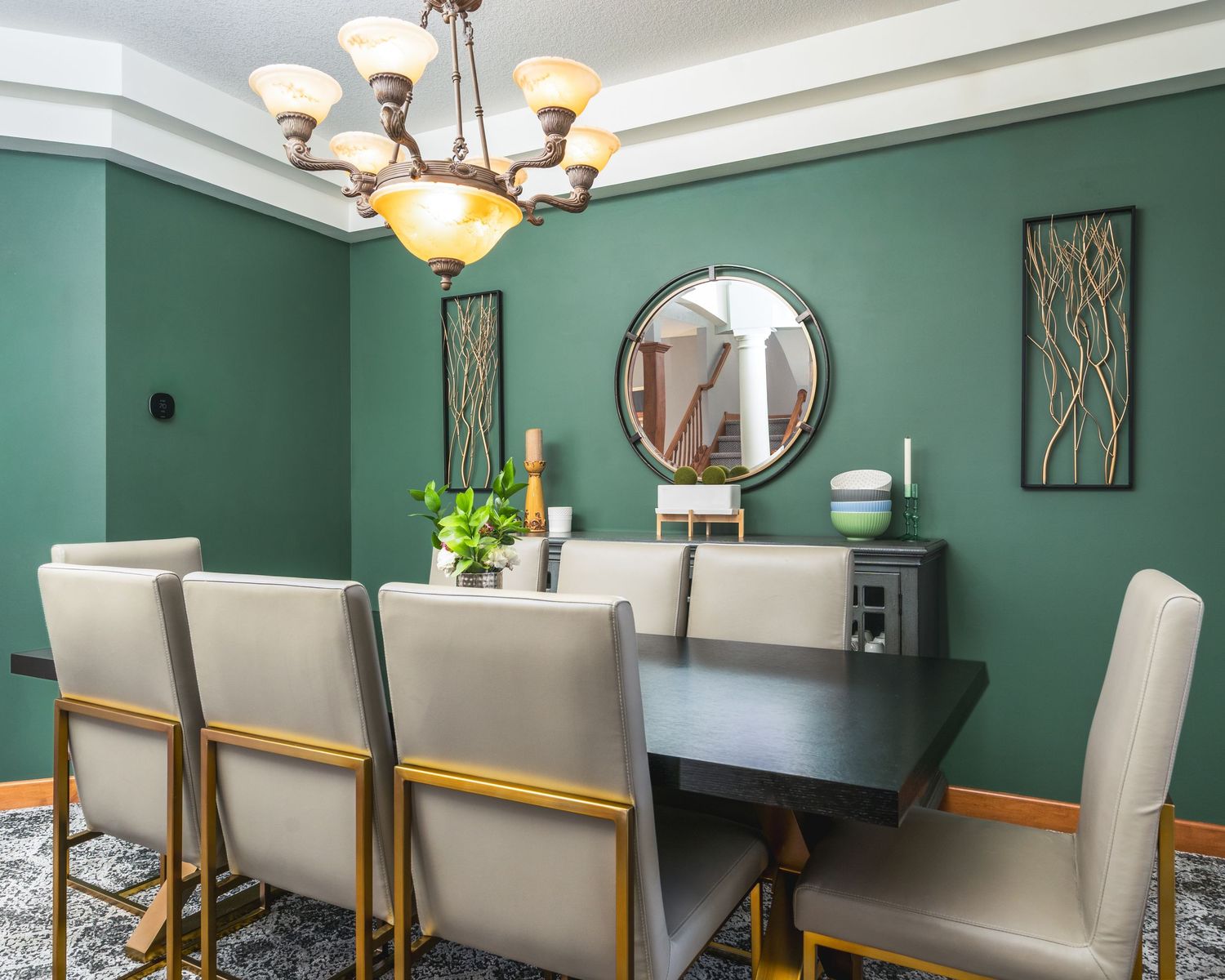 A modern dining room with teal green walls, upholstered chairs, and elegant chandelier lighting fixtures.