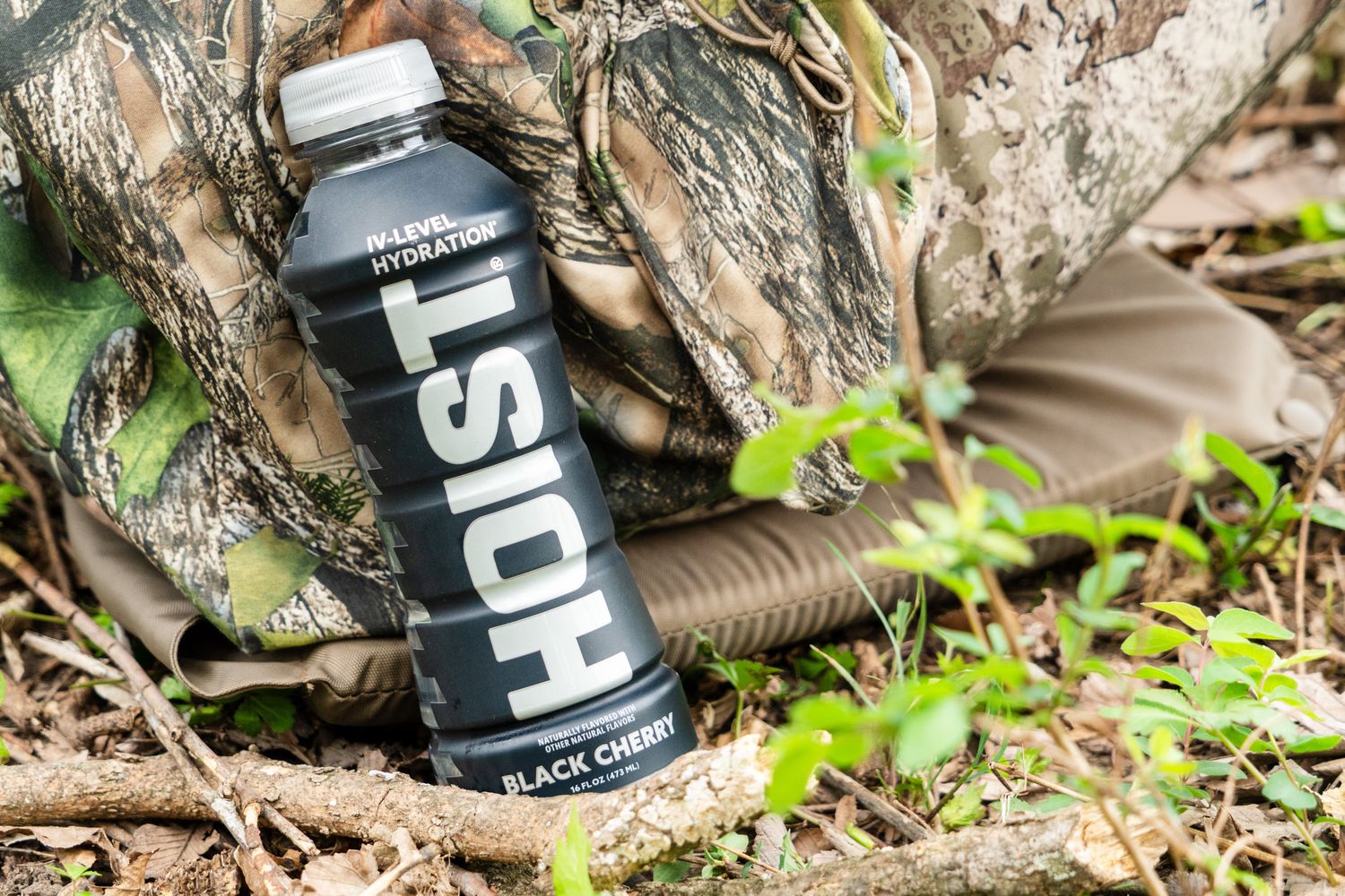 Black HOYT water bottle rests against tree trunk in outdoor setting.