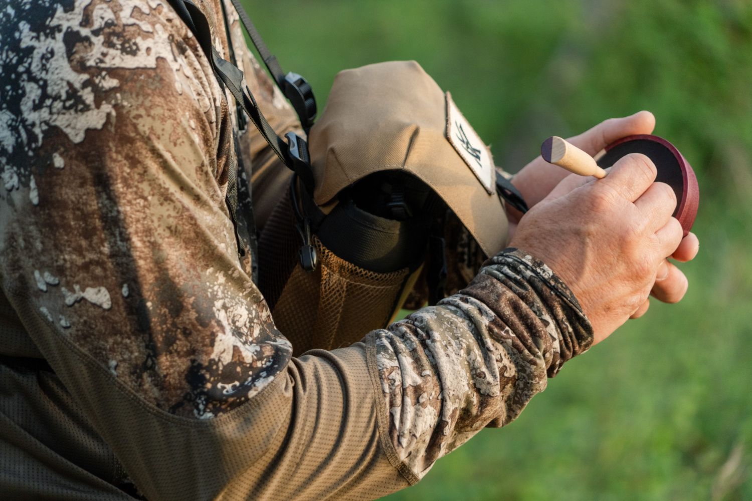 Detail shot of hunter in camouflage gear checking equipment in natural setting.