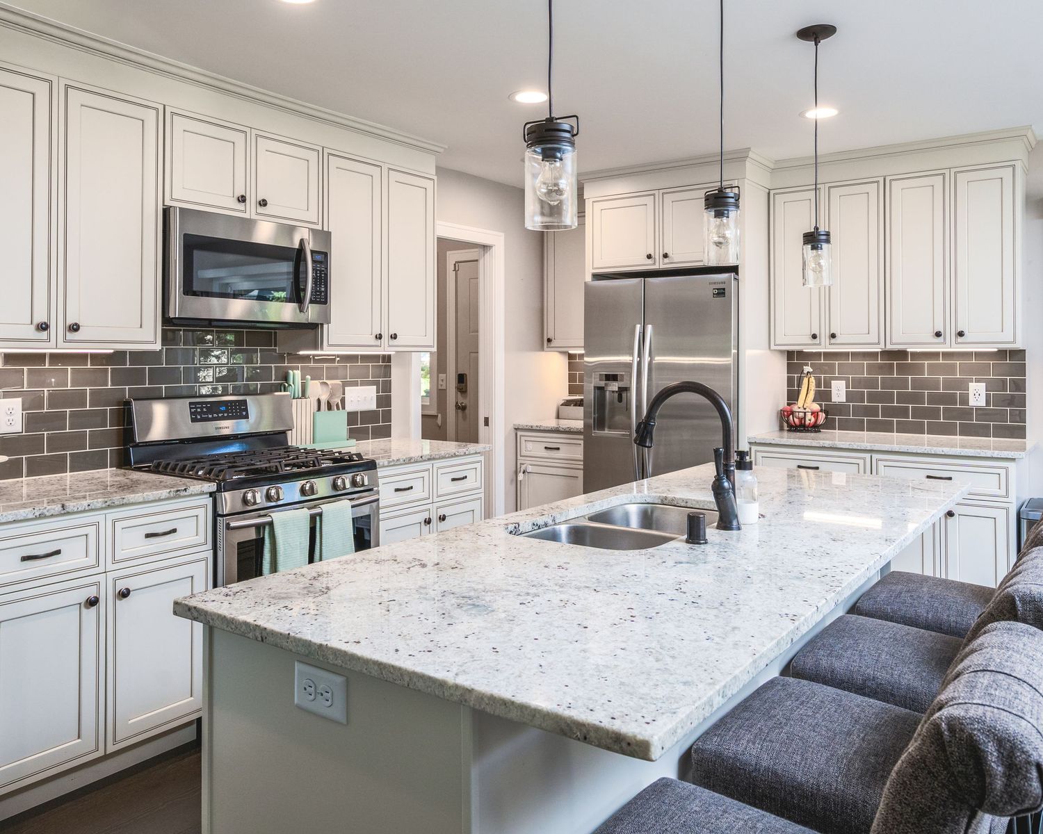 Modern white kitchen with granite countertops, subway tile backsplash, pendant lighting and large center island with seating.