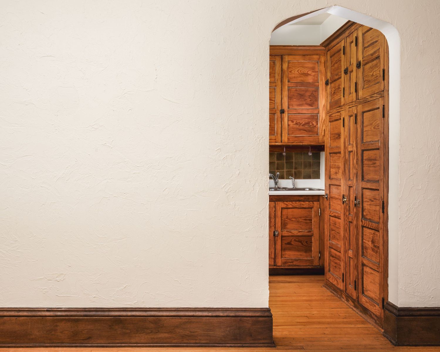 An arched wooden doorway with ornate panels leads into a room with built-in wooden cabinets and trim.