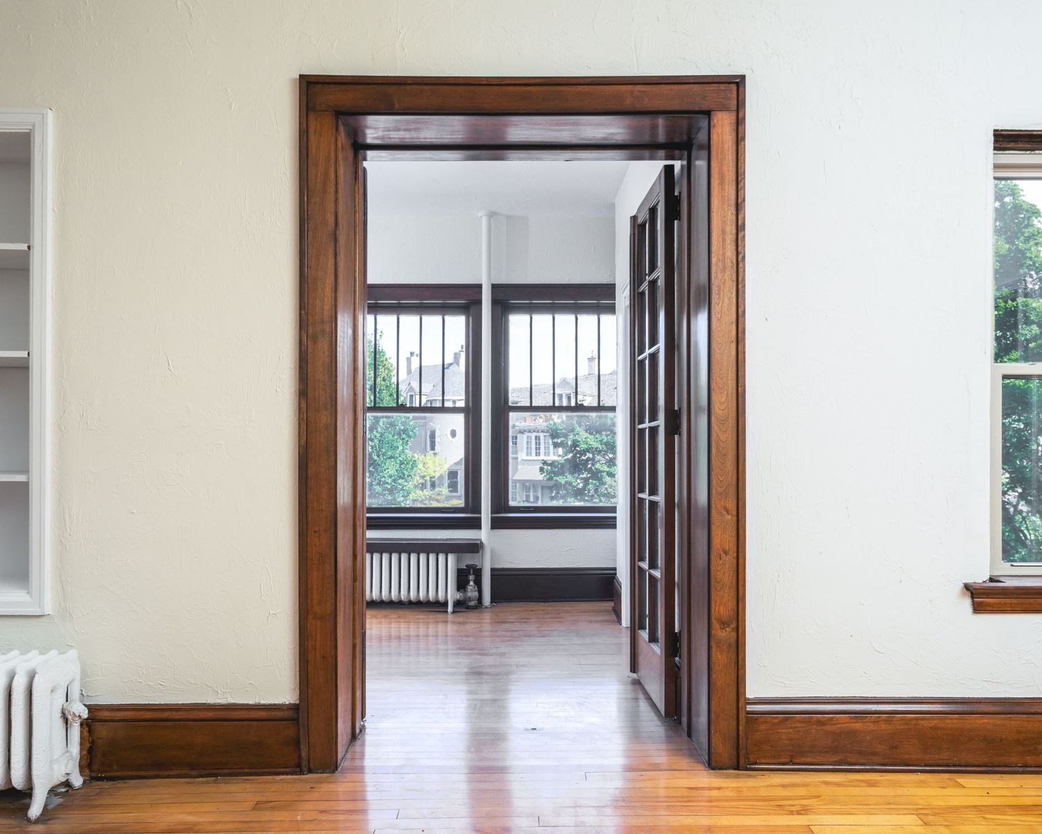 Interior doorway with dark wood trim leads to a sunlit room with hardwood floors and large windows.