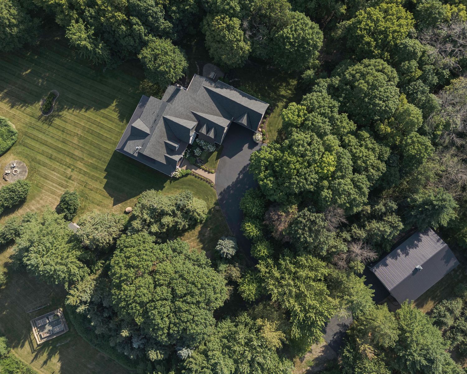 Aerial view of a large estate home surrounded by lush green trees and manicured lawn in a wooded setting.