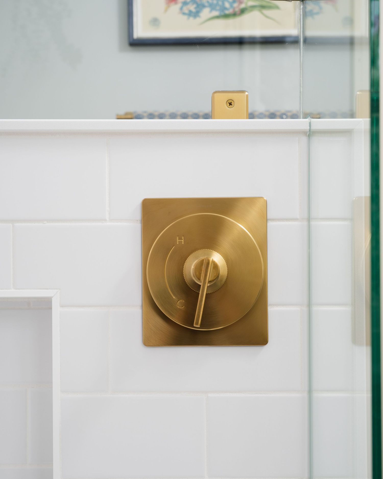 Brushed gold shower valve and handle on white subway tile wall in a modern bathroom.